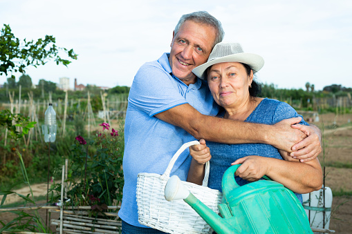 Portrait of happy cheerful elderly couple of amateur gardeners posing in homestead garden on sunny summer day