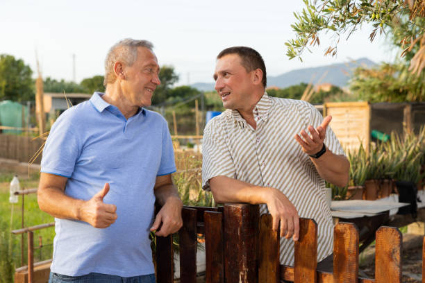 due giardinieri maschi che parlano amichevolmente accanto alla recinzione di legno della tenuta di campagna - vicino foto e immagini stock