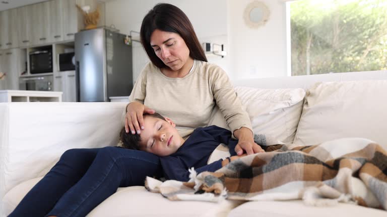 Loving mom caressing her sick son while he is lying down on the couch sleeping