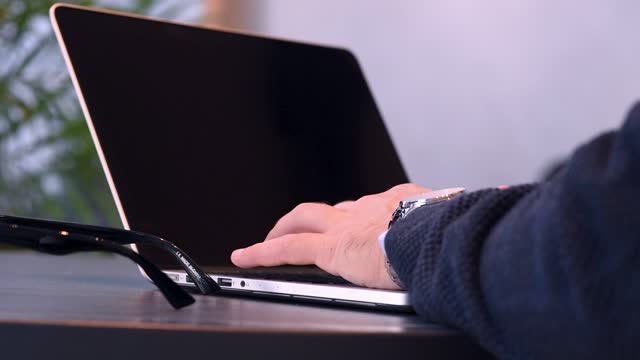 Close-up of a man typing on a laptop with a blank screen