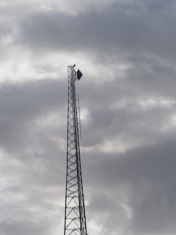 A radio frequency communications tower with multiple antennas with a stormy cloudscape background. Multiple antennas including microwave link are positioned on this tower. With room for copy.