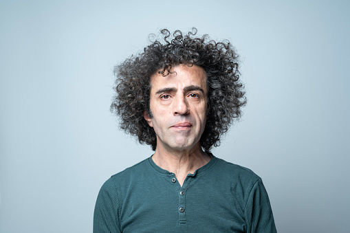 Portrait of mature adult man with long curly hair on gray background. He is wearing a green sweater. Shot in studio.