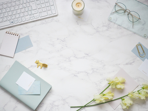 Refreshing copy space with blue stationery and yellow sweet peas on a marble desk