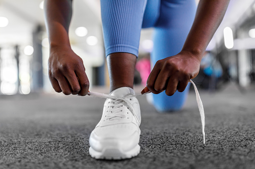 A close-up view of an African female sportswoman is tying shoelaces in a modern gym.