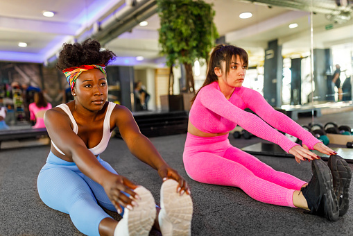 An attractive young African-American woman is doing push-ups in a gym with her female friend.