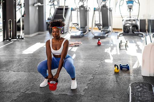 A beautiful young African woman is doing exercise training in a gym using dumbbells.