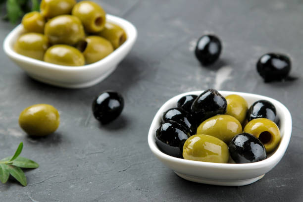 istock Green and black olives in a white ceramic bowl with leaves on a dark graphite background. close-up 1447524874