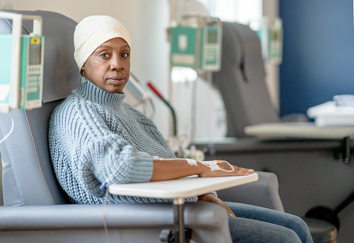 An older woman wearing a head scarf sits patiently as she receives her IV drip.