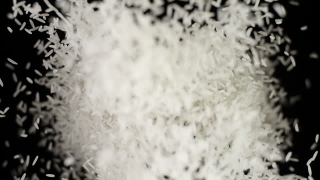 Rice seeds bouncing against camera black background, grains flies slow motion