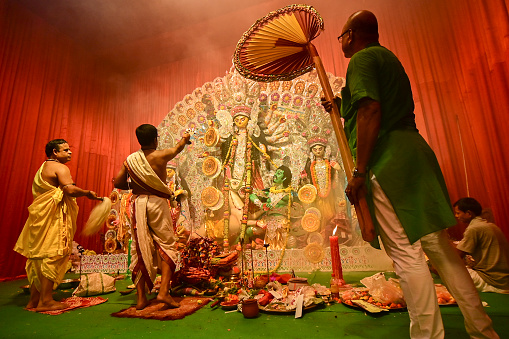 Howrah, India -October 13, 2021 : Hindu Priests worshipping Goddess Durga with panchapradip, ghanta, chamor and hand fan. Ashtami puja aarati - sacred Durga Puja ritual - shot at night.