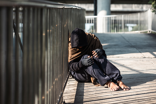 Poor tired stressed depressed hungry homeless man in the shadow city. Homeless man sitting on the street waiting for help food and money from people volunteer foundation donate.