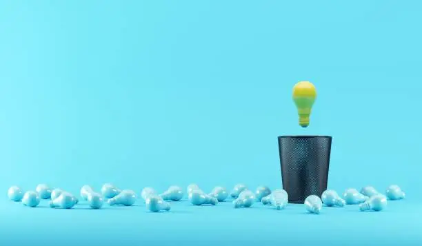 Photo of Lighting bulb floating on Bin Trash with Blue illumination bulb placed on a blue background. 3D render. minimal creative idea.