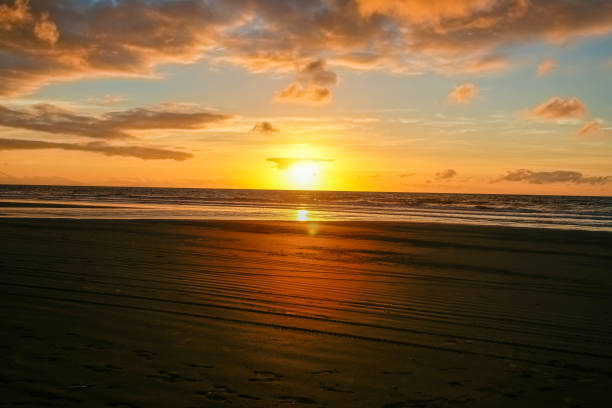 istock Beach in silhouette as sunsets on distant horizon over ocean. 1447556031