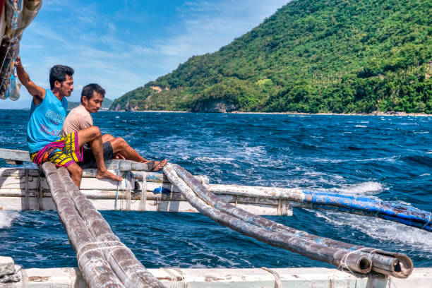 dos miembros de la tripulación local de banca viajan en un estabilizador mientras conducen a lo largo de la isla de mindoro, filipinas. - motoring fotografías e imágenes de stock