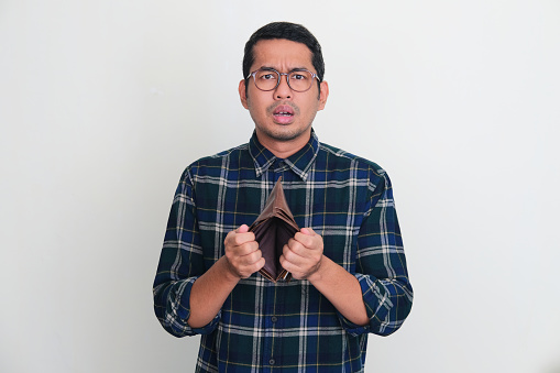 Adult Asian man looking camera with sad expression while showing his empty wallet