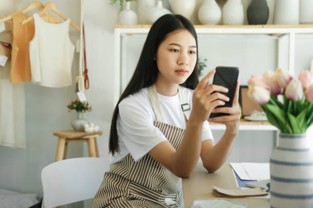 istock Young asian business owner holding phone and retail package parcel. 1447560593