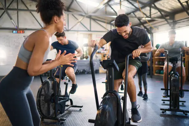 Photo of Cycle exercising, fitness and applause of a coach with motivation for cycling gym training. Sports coach clapping for workout, wellness and bike exercise success of people on bicycle happy from cardio