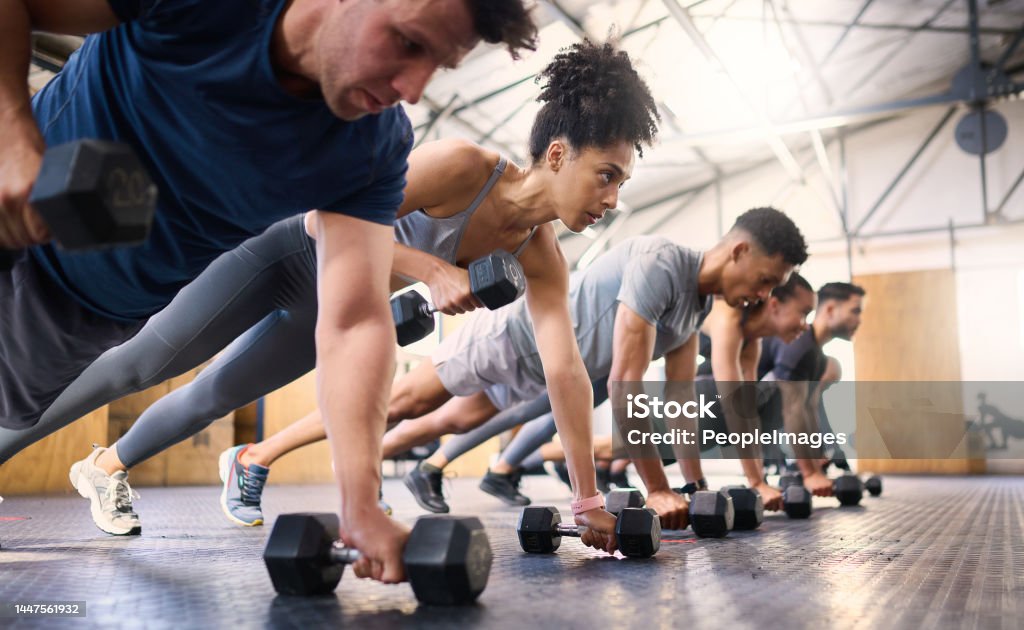 Strong, fitness and gym people with dumbbell teamwork training or exercise community, accountability and group. Sports diversity friends on floor in pushup muscle workout, power and wellness together Exercising Stock Photo