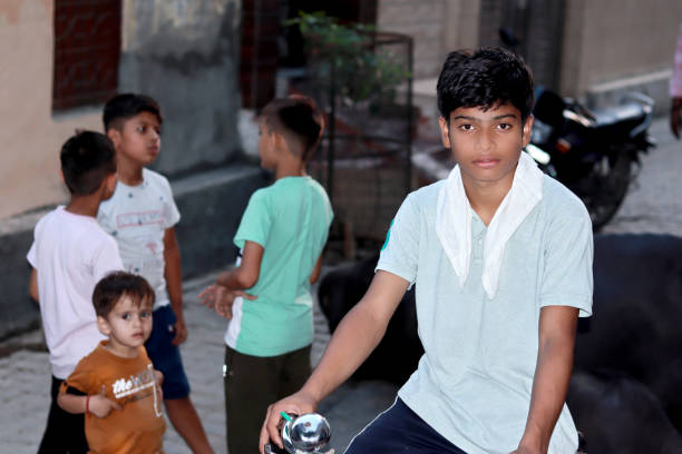 Teenage boy of Indian ethnicity standing with cycle and some of small boys standing behind him.