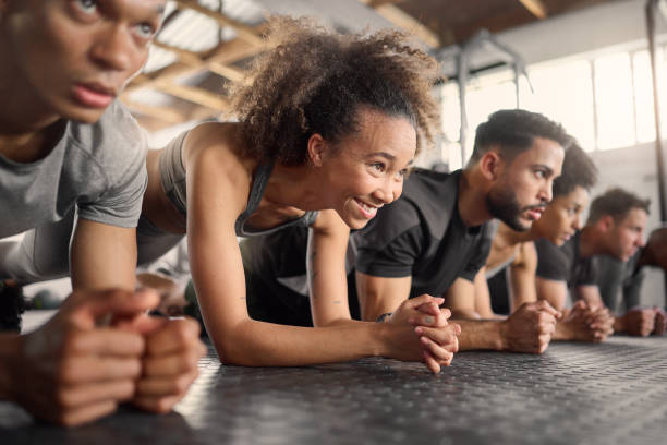 fitness, femme et exercice de planche dans le gymnase d’entraînement en groupe pour le bien-être, un mode de vie sain et l’entraînement. forte, jeune et heureuse fille noire, athlète et au sol poussent avec des amis pour un défi sportif - core workout photos et images de collection