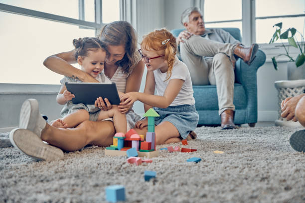 mutter, kinder und digitales tablet im wohnzimmer mit familie entspannen, spielen und verbinden sich in ihrem zuhause zusammen. lernen, kinder und mama schauen online-spiel, cartoon und unterhaltung mit mädchen auf teppich - senior adult digital tablet domestic life learning stock-fotos und bilder