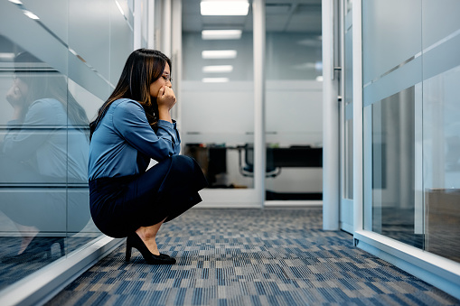 Stressed out Asian businesswoman crouching in hallway on an office building. Copy space.