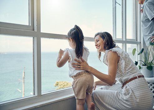Family view, window and mother with child bonding, having fun and enjoy quality time together in home living room. Mama's love, happiness and mom with kid girl watch the ocean through glass window