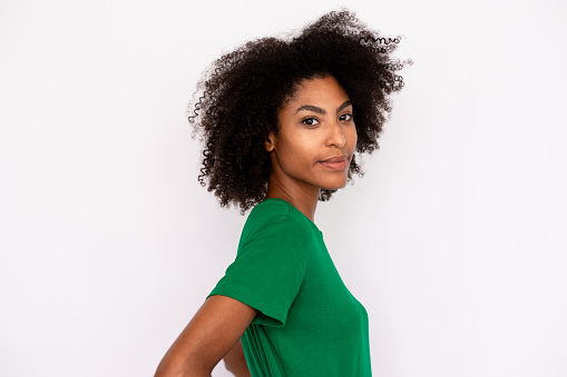Portrait of serious young woman looking at camera. African American lady wearing green T-shirt and jeans posing over white background. Female beauty