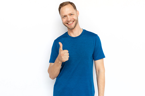 White man showing thumb up at camera and smiling. Happy adult man looking at camera, standing on white background and showing approving gestures. Agreement, approval concept