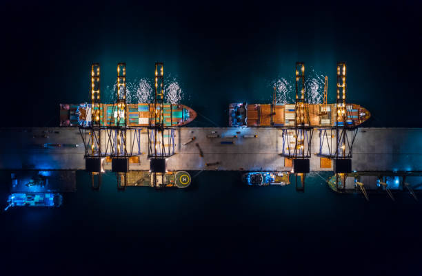 Aerial top view of international port with crane loading containers in import export business logistics. Container loading and unloading cargo freight ship in deep sea at night. stock photo