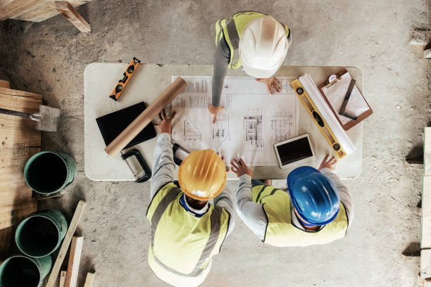 vista superior, trabajadores de la construcción o planificación de planos en la casa, el hogar o el edificio de oficinas en bienes raíces, propiedad o innovación arquitectónica. hombres, mujeres ingenieras o personas o ideas del sitio de construcción - construccion fotografías e imágenes de stock