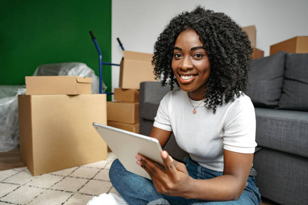istock Young African woman using a tablet as she sits in living room surrounded by cardboard boxes 1447583247