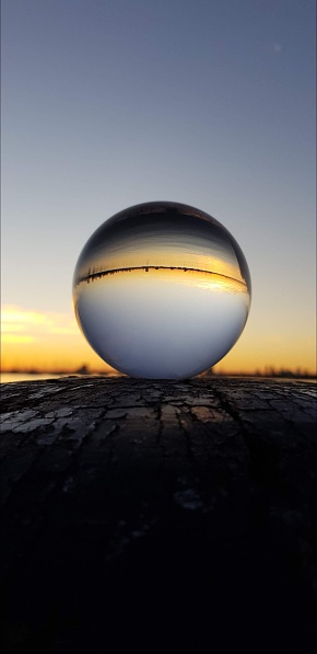 A vertical shot of a lens ball inversely reflecting a sunset sky across a lake