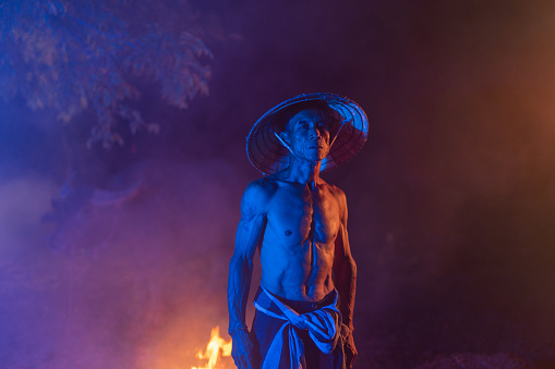 Asian village lifestyle concept of Thailand, portrait of a buffalo breeder worker with his buffalo during a cold winter foggy night in Sakon Nakhon, Northeast Thailand, Isan way of life.