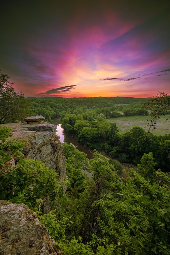 A vertical shot of strea flowing through rock formations and lush green trees during sunset