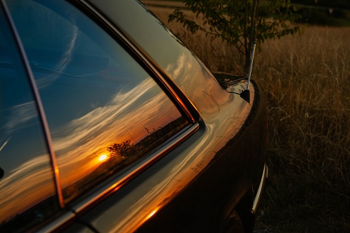 The sun during sunset reflecting in old car window with a field in the background