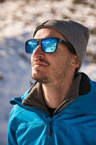 A vertical shot of a male with blue sunglasses reflecting the snowy mountains