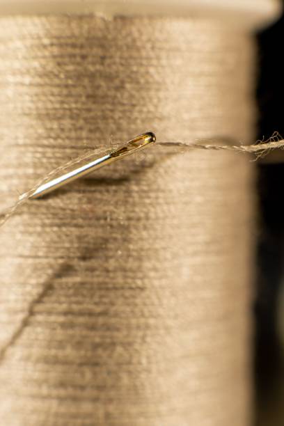 istock Vertical closeup of a needle with a long brown thread going through its hole in front of the yarn 1447591555