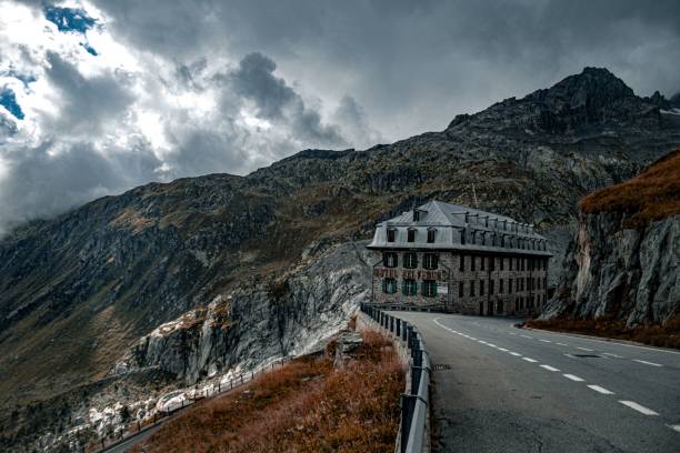 Low-angle of Furka Pass autumn view with a building yellow grass mountains gloomy sky background A low-angle of Furka Pass autumn view with a building yellow grass mountains gloomy cloudy sky background furka pass photos stock pictures, royalty-free photos & images