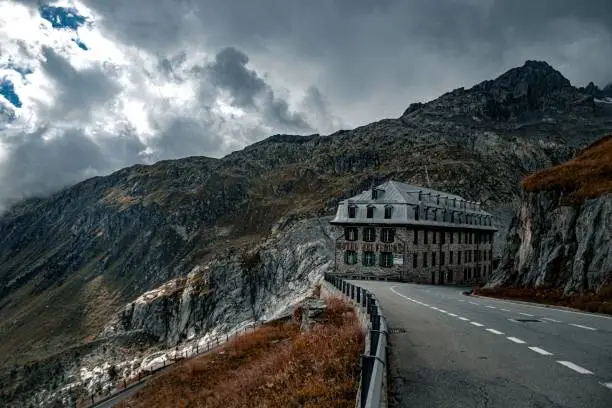 A low-angle of Furka Pass autumn view with a building yellow grass mountains gloomy cloudy sky background