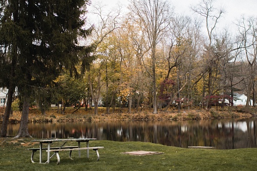 A picnic table near a calm, reflective lake surrounded by colorful trees during the fall in Morris County, New Jersey
