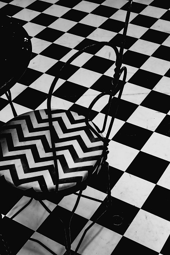 A vertical shot of a black and white chevron chair on a black and white checkered pattern floor.