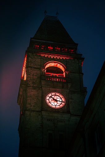 A vertical shot of a medieval clocktower with red lighting against the night sky