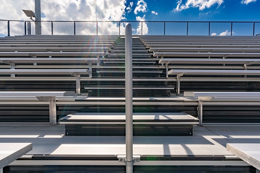 Looking up at anticipation of climbing exterior stadium bleacher stairs with a sun star near the top with clouds. Nondescript location with no people