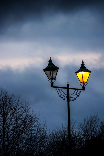 A vertical shot of a vintage street lamp against the background of the cloudy sky.
