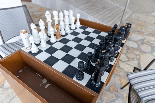 A close-up of a chess board with arranged chessmen, and chairs placed against each other