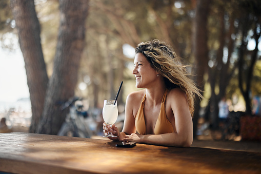 Young happy woman enjoying while drinking fresh lemonade on the beach in a café. Copy space.