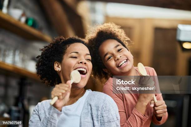 Happy Black Mother And Daughter Singing With Wooden Spoons At Home Stock Photo - Download Image Now