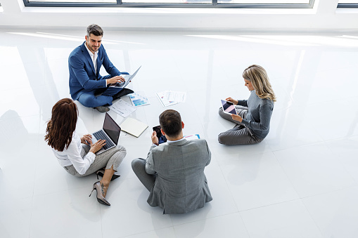 High angle view of group of entrepreneurs talking while working on wireless technology on floor at casual office. Copy space.