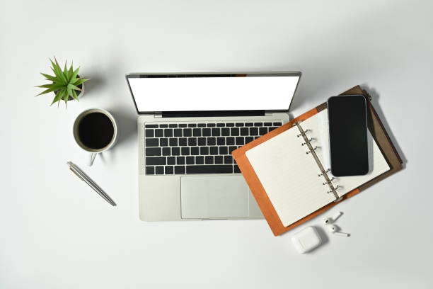 istock White office desk with laptop, notepad, mobile phone and coffee cup. Top view modern workplace. 1447609854